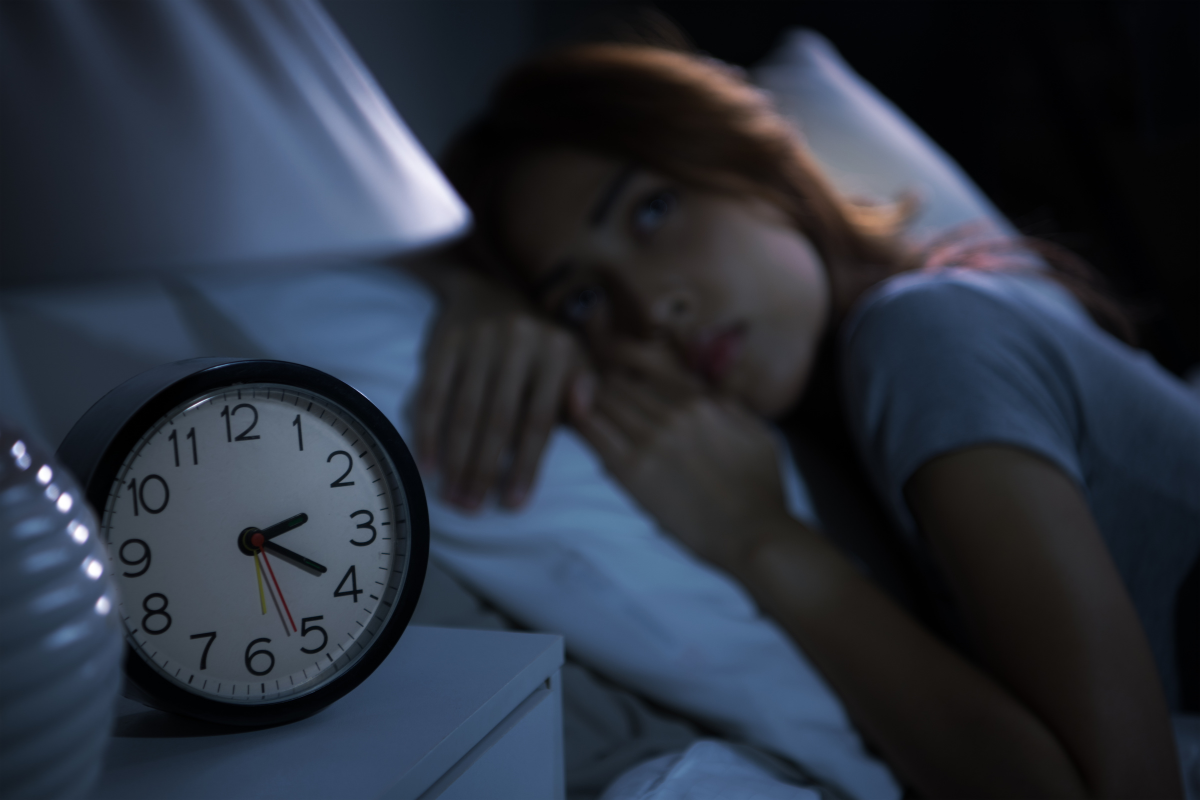 Woman lying in bed with a worried expression, clock showing late hour, symbolizing sleep disruptions and insomnia for Ankeny residents.