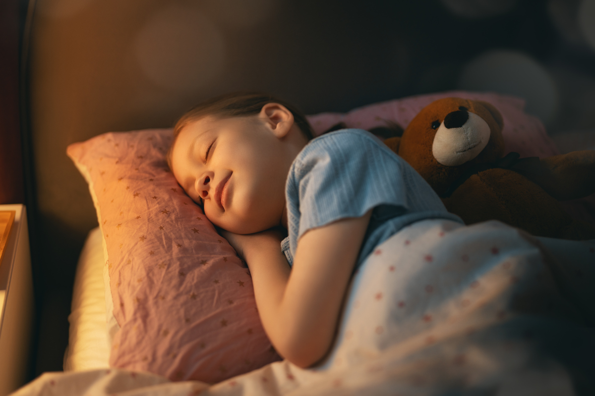 Child peacefully sleeping with teddy bear in a cozy bedroom, illustrating the importance of a relaxing sleep routine for children in Sioux Falls.
