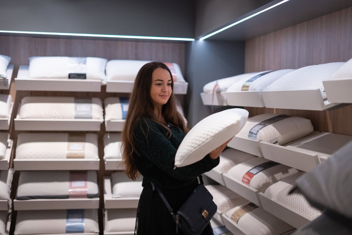 Woman selecting a pillow in a store, surrounded by various pillow options, emphasizing the importance of choosing the right pillow for individual sleep styles.