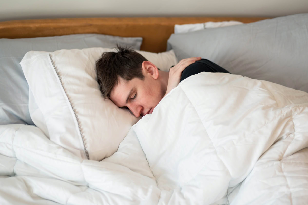 Person sleeping peacefully under a cozy white comforter in a warm bedroom, illustrating tips for improving sleep quality during Sioux Falls winters.