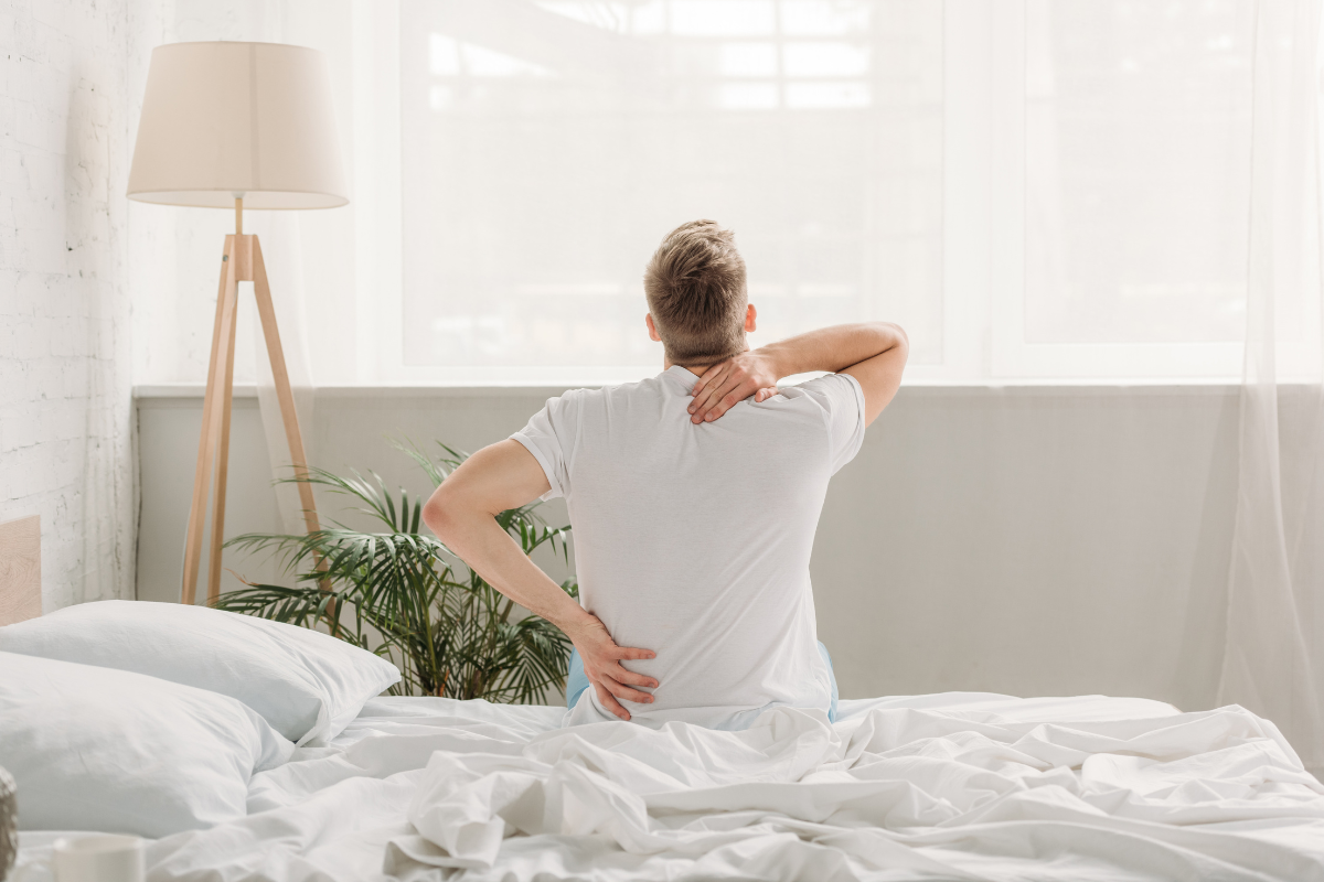 Man sitting on a bed, experiencing back pain, with a focus on spinal alignment and mattress comfort, highlighting the connection between mattress choice and back pain relief.