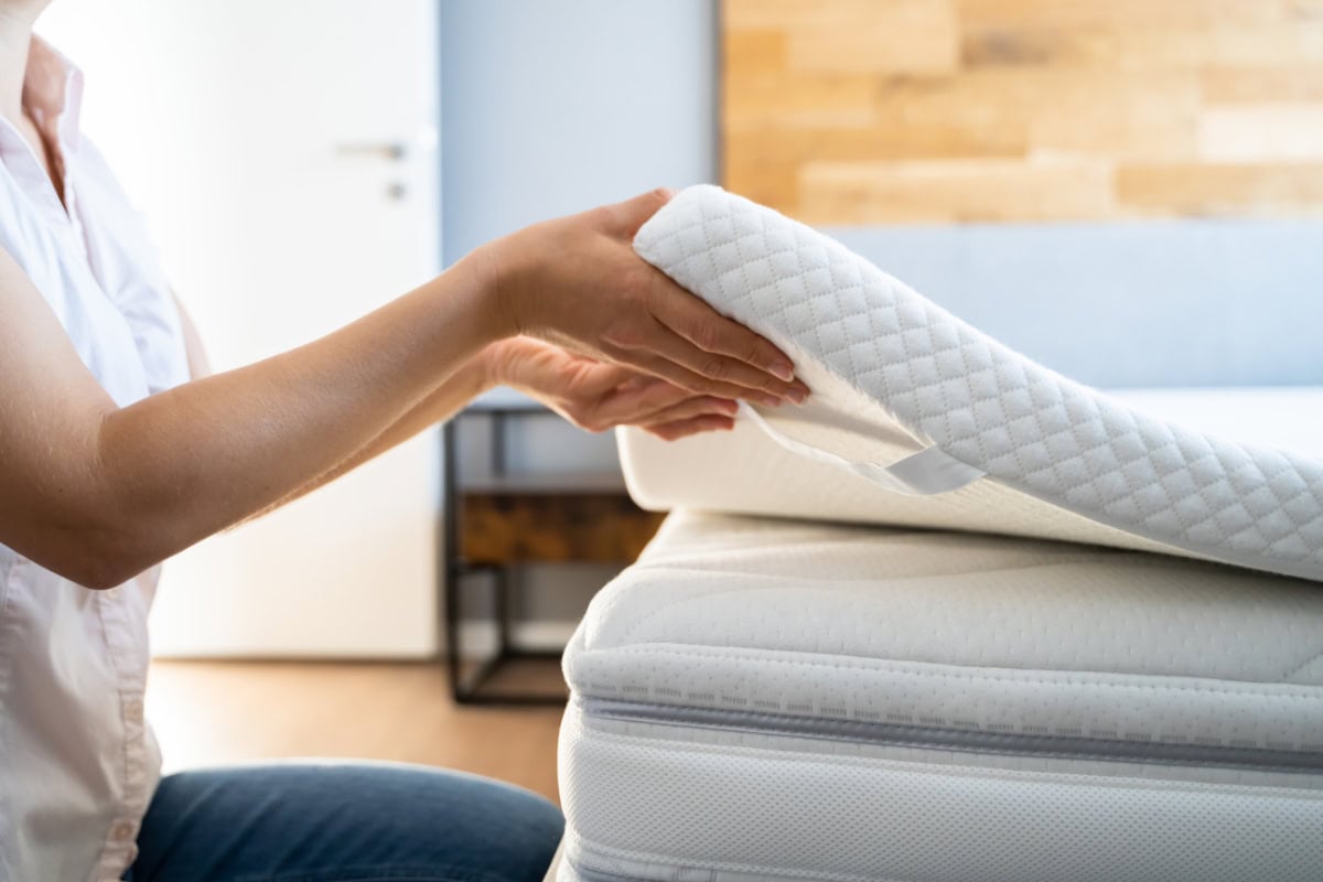 Person placing a bed topper on a mattress, demonstrating comfort enhancement for better sleep quality.