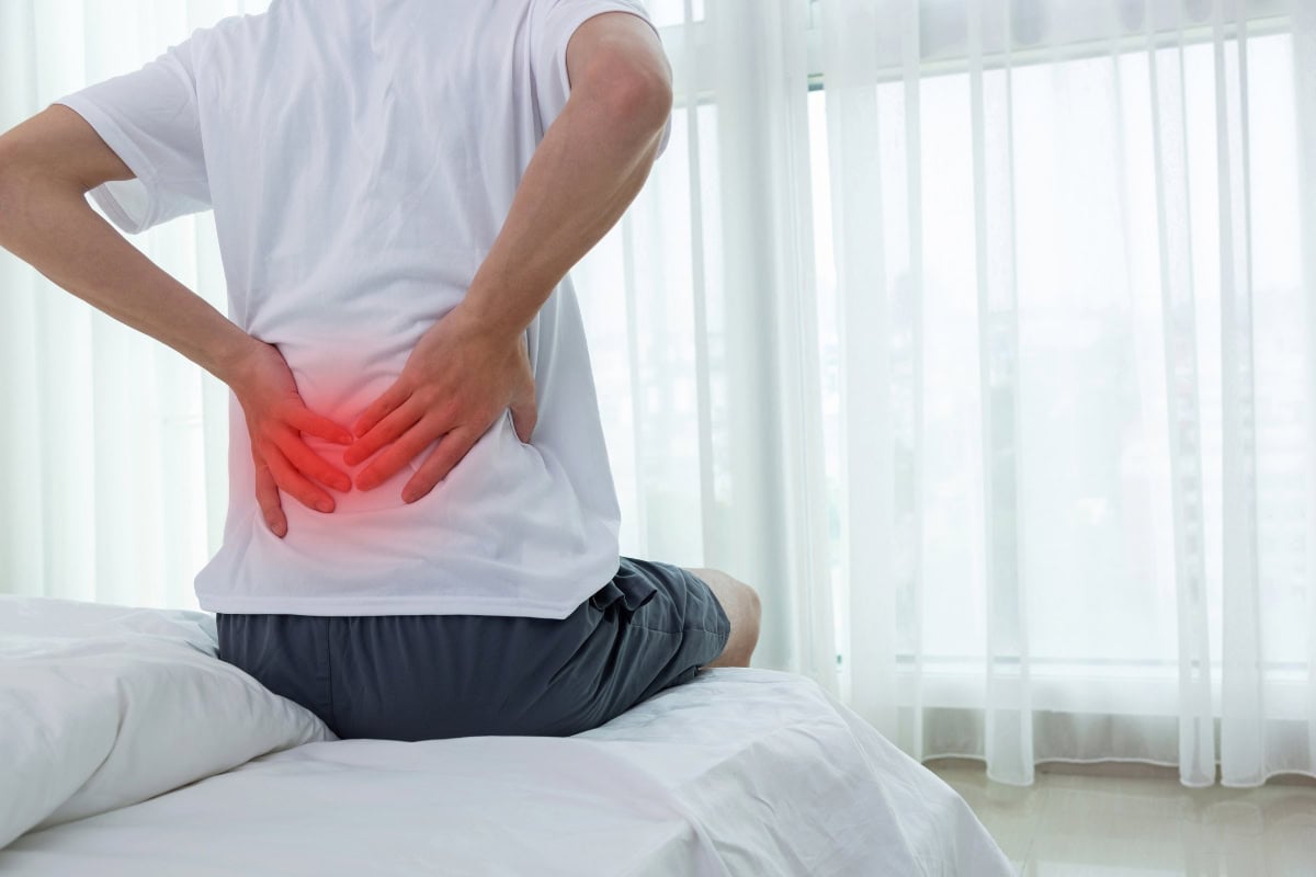 Person experiencing back pain while sitting on a bed, highlighting the importance of foam mattress toppers for back pain relief and improved sleep quality.