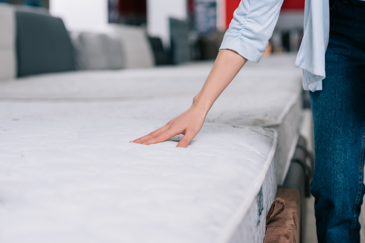 Person examining a mattress in a showroom, focusing on its surface texture, relevant to selecting the best mattress for individual needs.